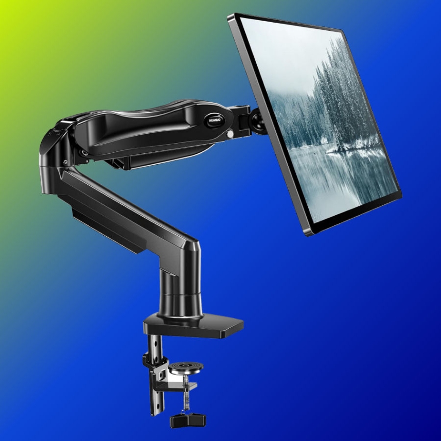 A monitor held on the HUANUO single arm, clamped at the desk edge and pushed back to leave clear desk depth in front of the screen.